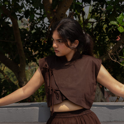 Woman wearing a brown outfit standing outdoors with greenery in the background