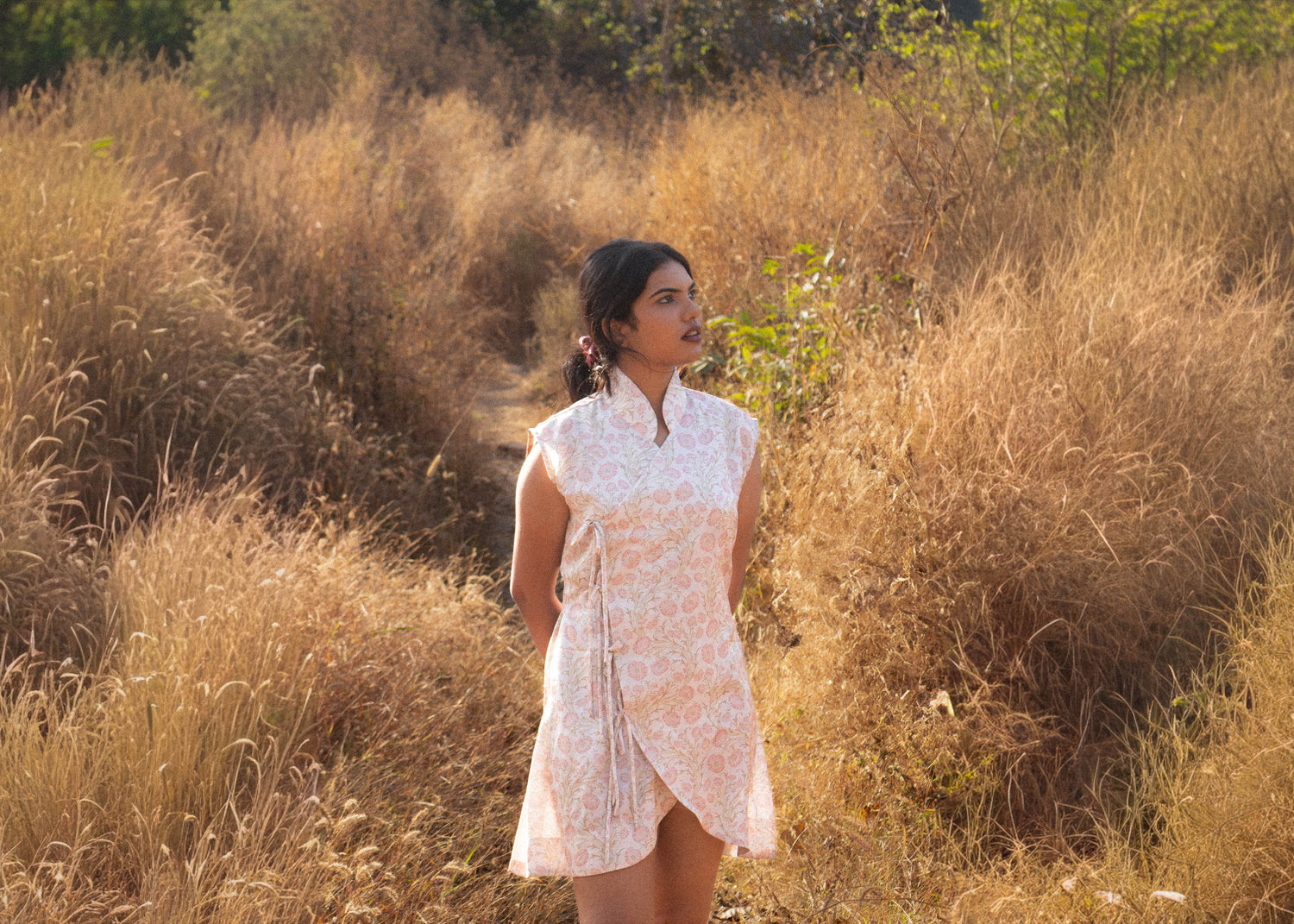 Woman in a white dress standing in a field of tall, dry grass.