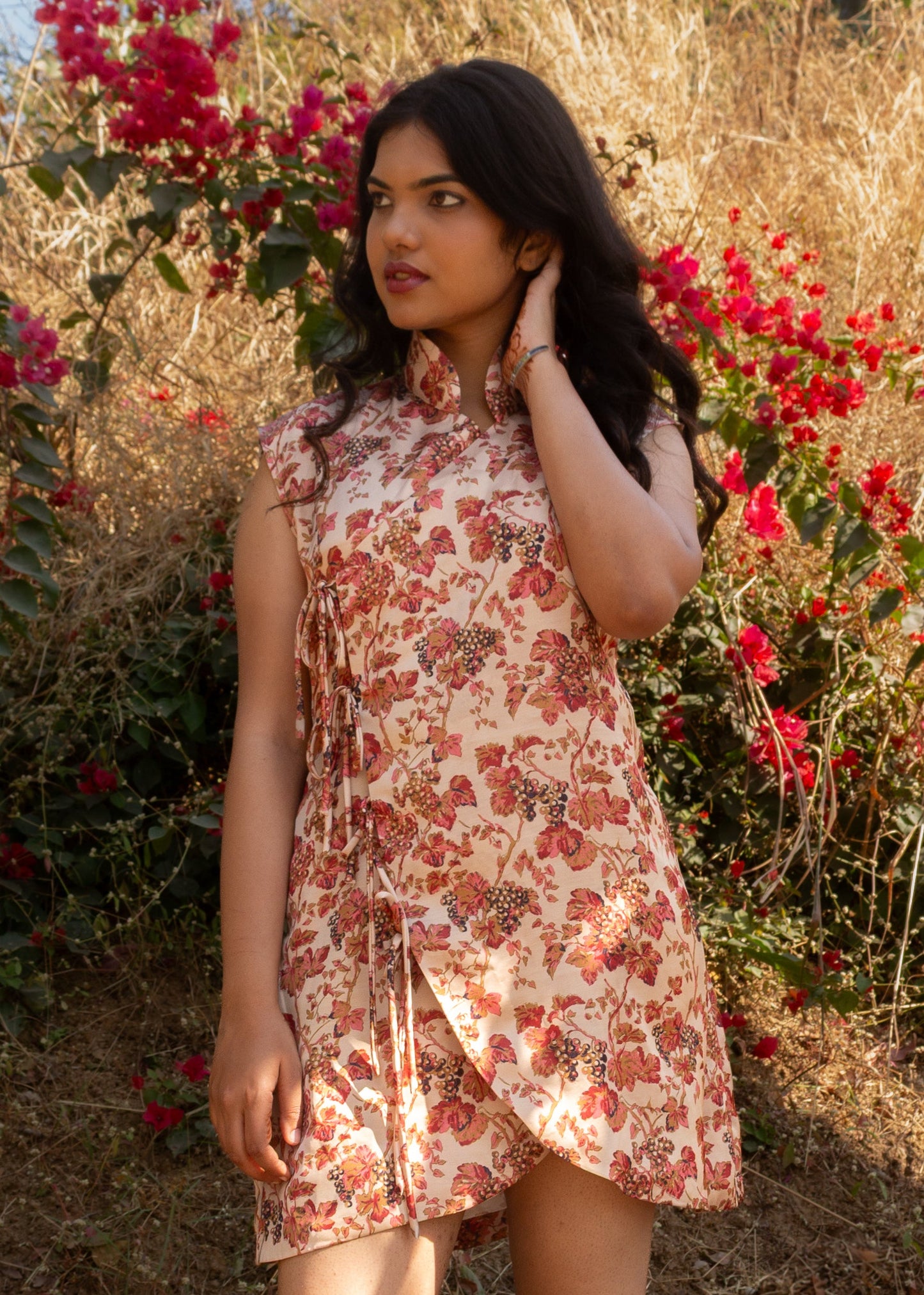 Woman in a floral dress standing among red flowers and dry grass.