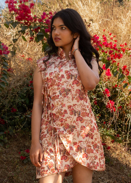 Woman in a floral dress standing among red flowers and dry grass.
