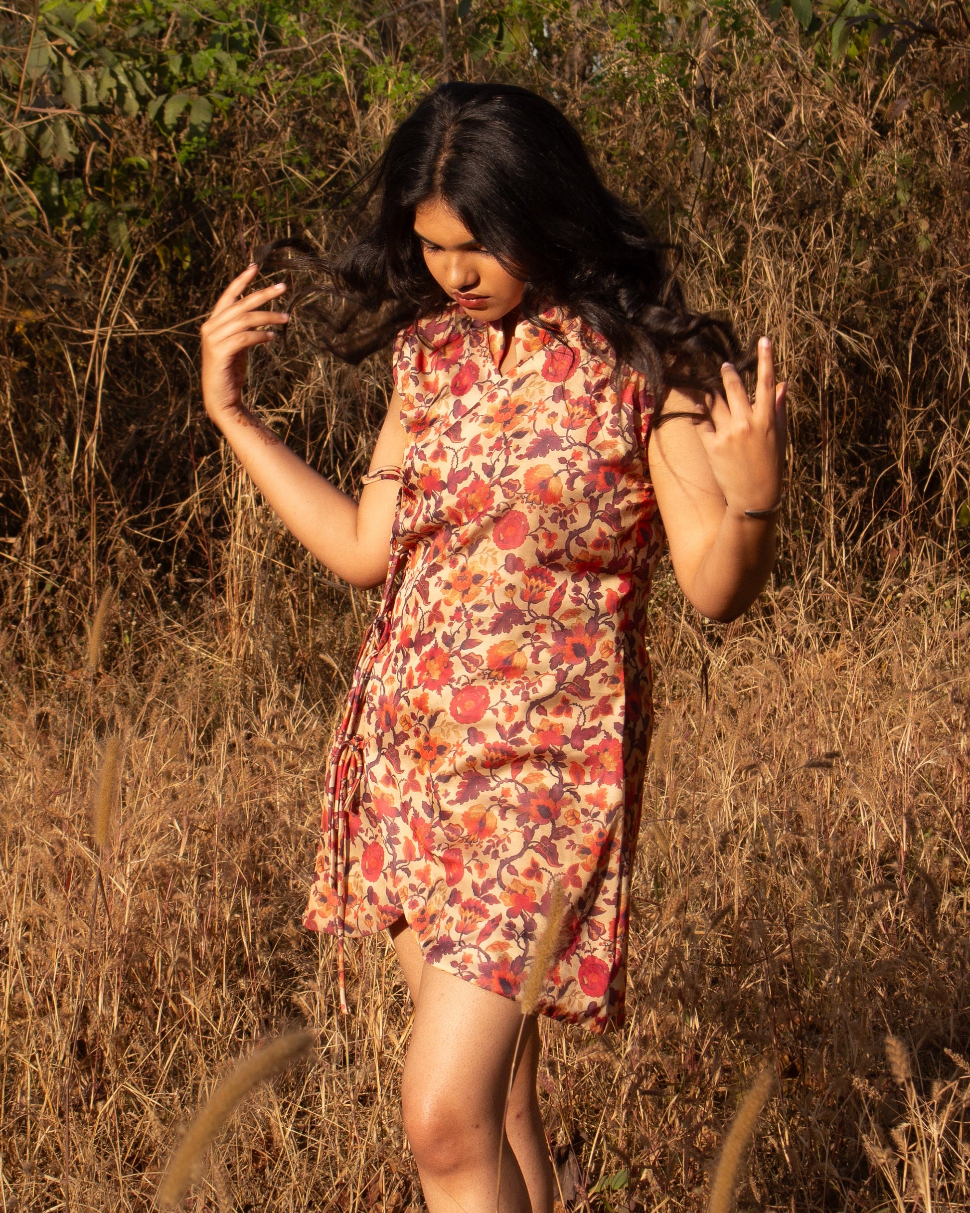 Woman in a floral dress standing in a field with dry grass and plants.