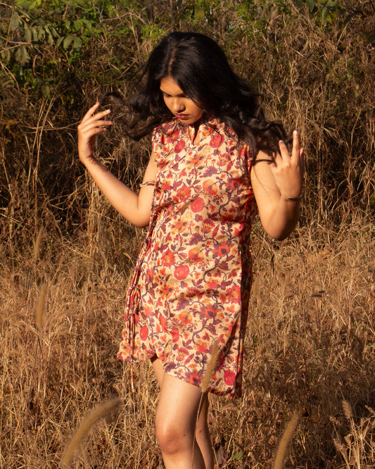Woman in a floral dress standing in a field with dry grass and plants.