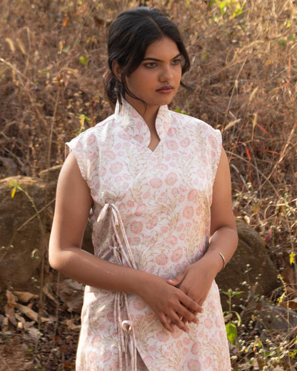 Woman wearing a light pink floral dress standing in a natural setting with dry grass and rocks.