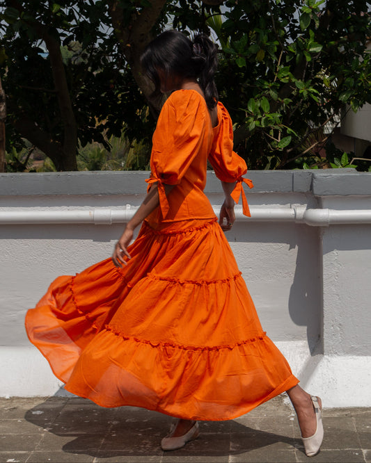 Woman in an orange dress standing outdoors with greenery in the background