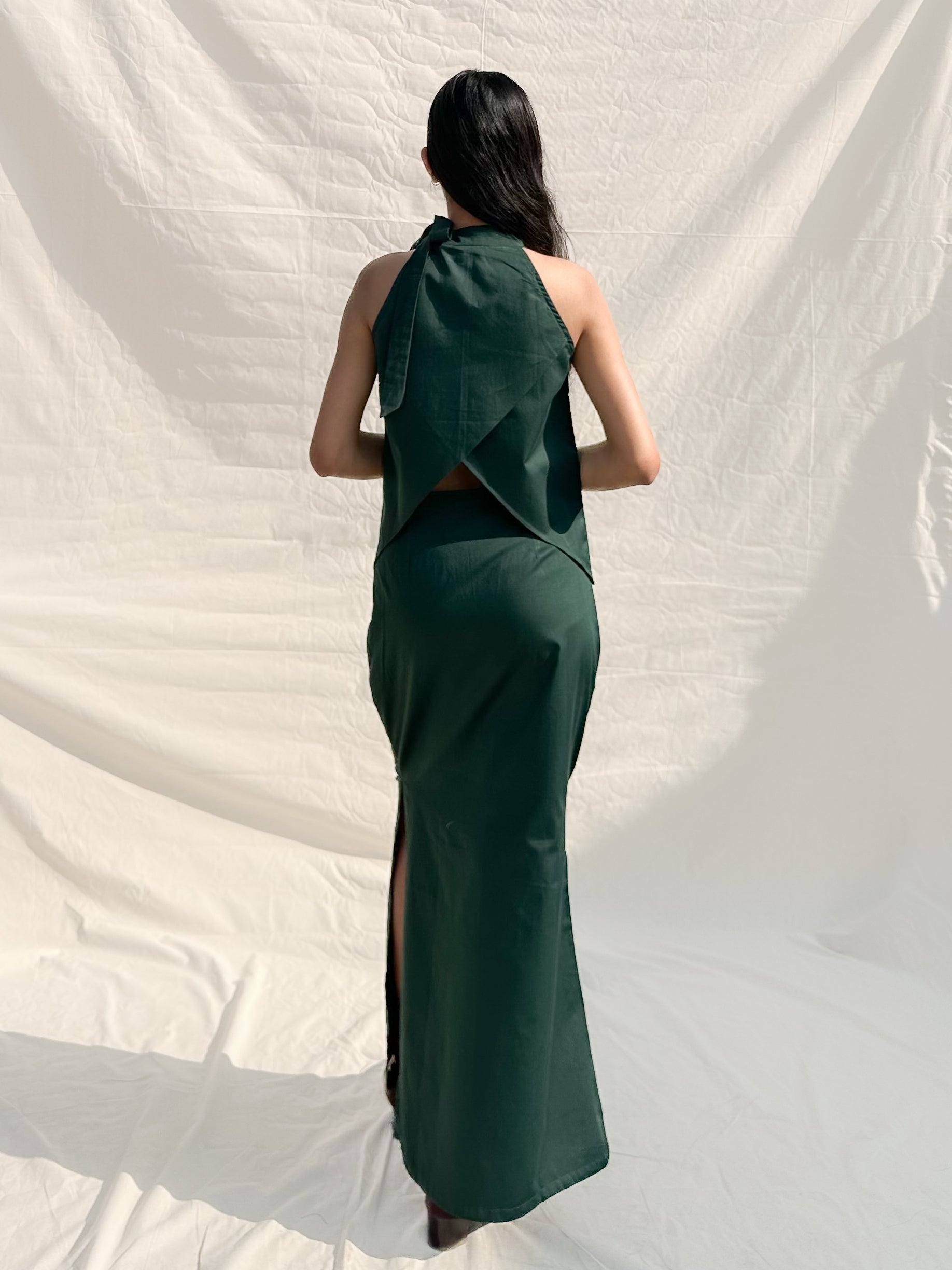 Woman wearing a green dress with a slit, standing against a white backdrop