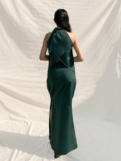 Woman wearing a green dress with a slit, standing against a white backdrop