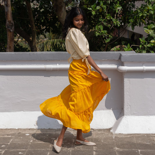 Woman in a yellow skirt and white top standing outdoors with greenery in the background