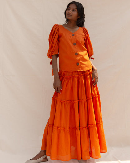 Woman wearing an orange outfit with a tiered skirt and puff sleeves against a plain background