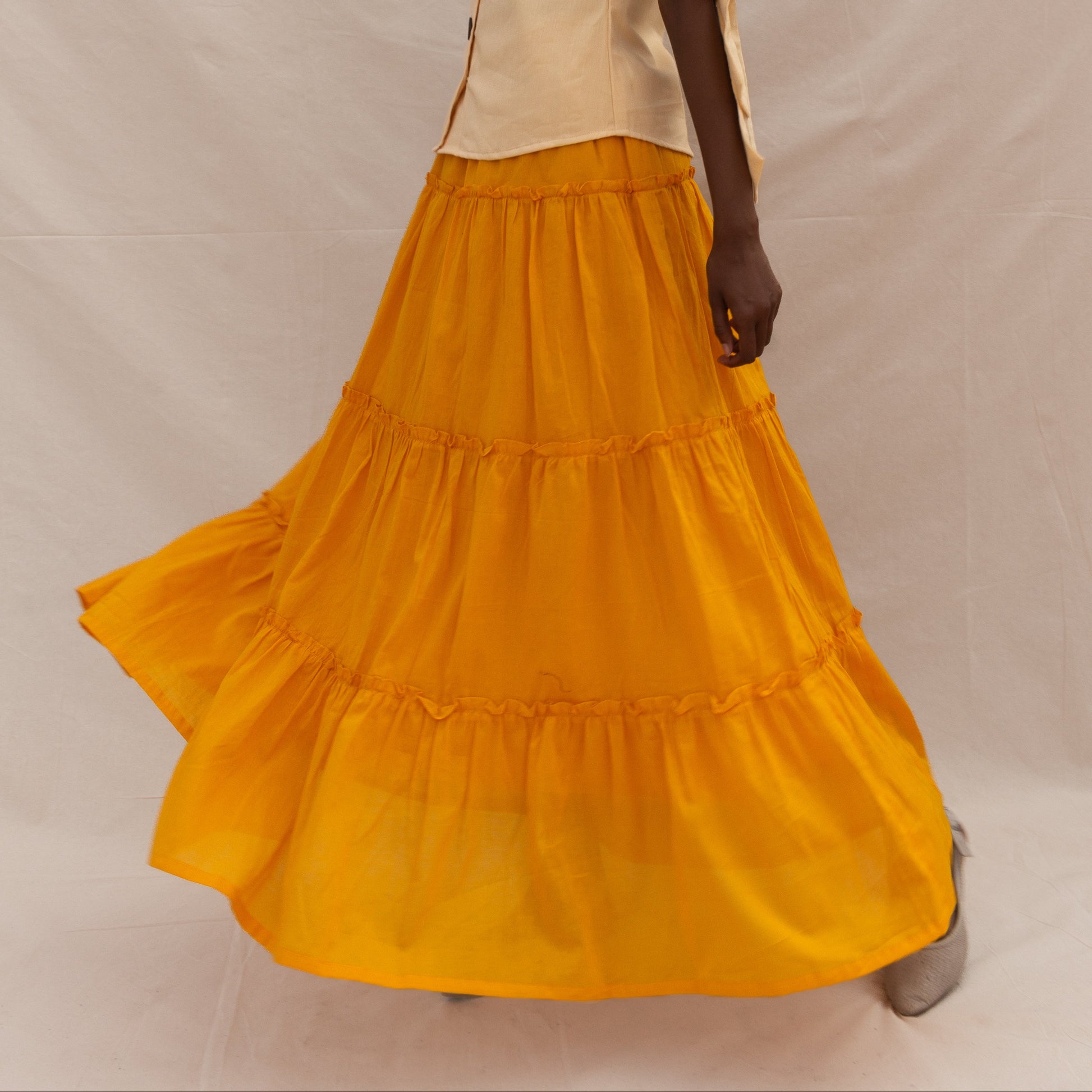 Person wearing a yellow tiered skirt and beige top against a plain background