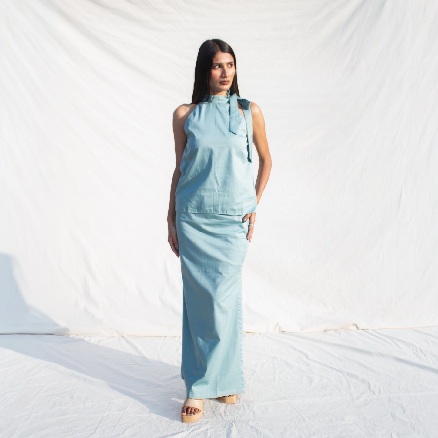 Woman wearing a light blue sleeveless top and pants on a white background