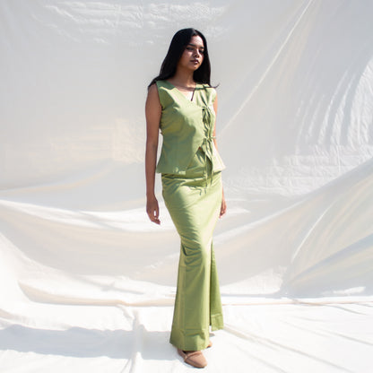 Woman wearing a green outfit standing against a white draped fabric background