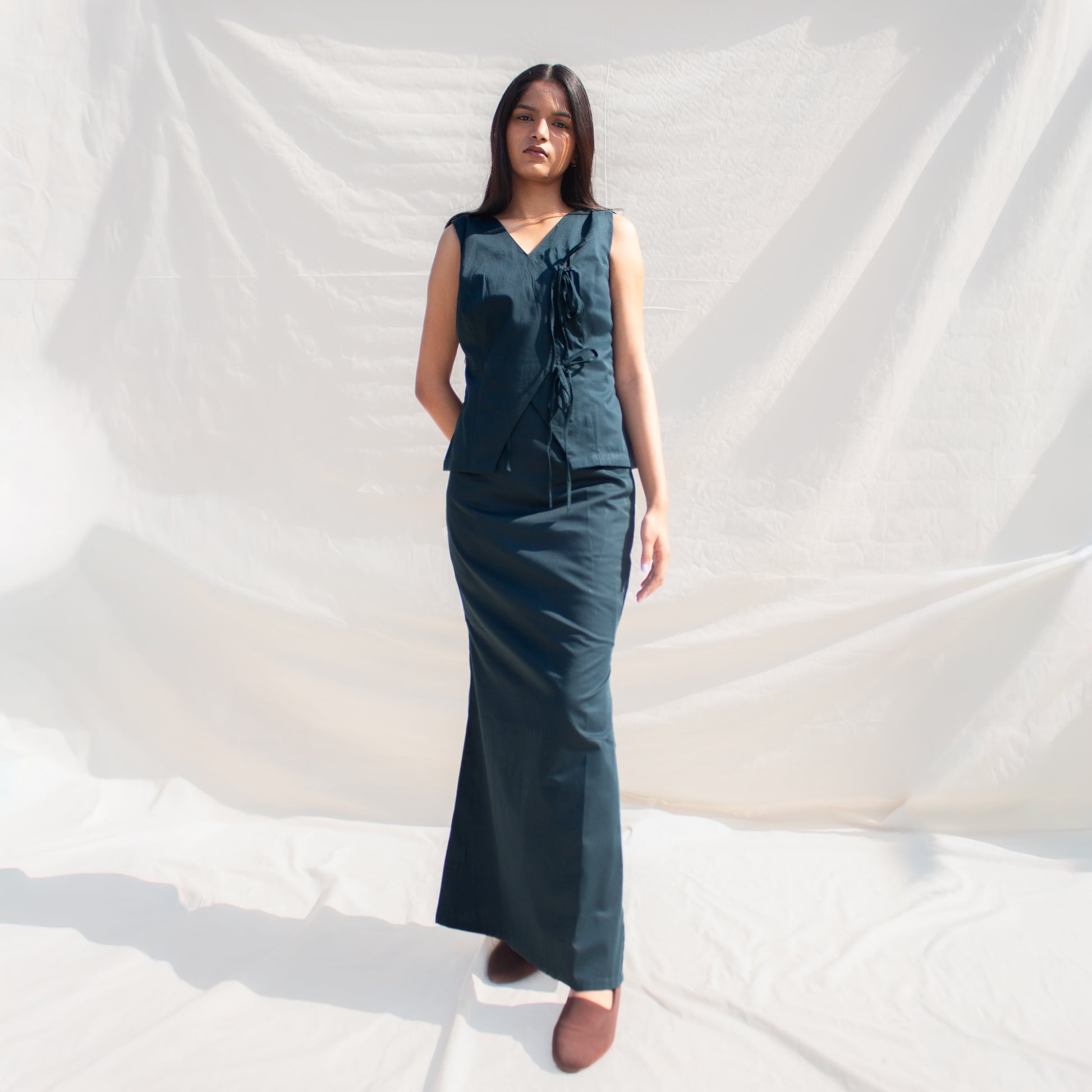 Woman wearing a dark green sleeveless top and long skirt against a white background