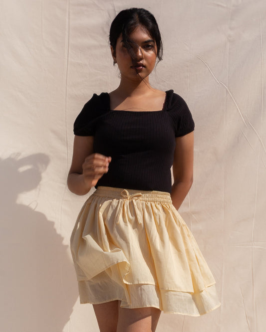 Woman wearing a black top and yellow skirt against a beige wall