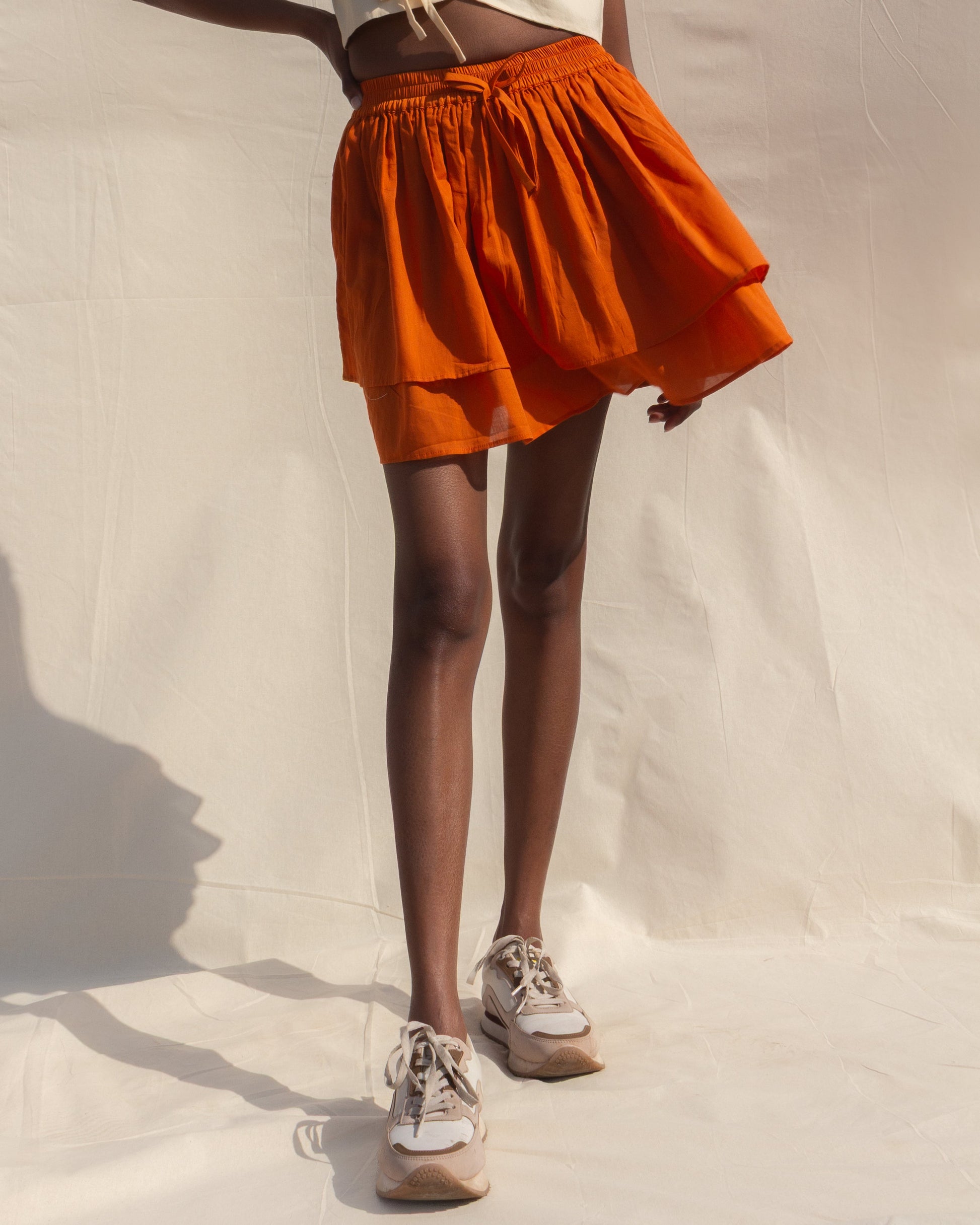 Person wearing an orange skirt and white sneakers on a neutral background