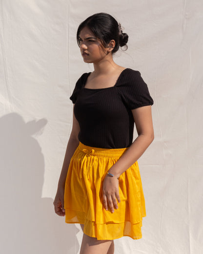 Woman wearing a black top and yellow skirt against a white background