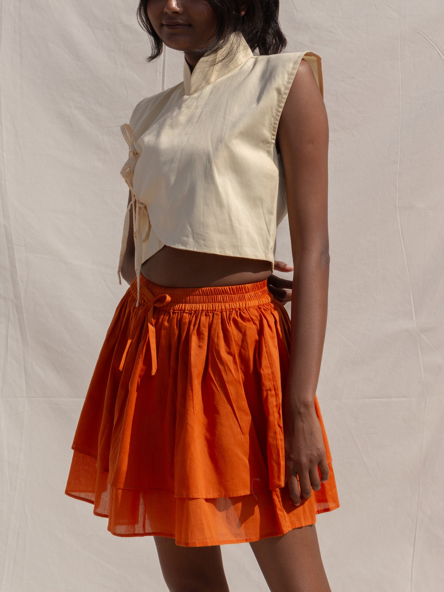 Person wearing a white sleeveless top and orange skirt against a plain background