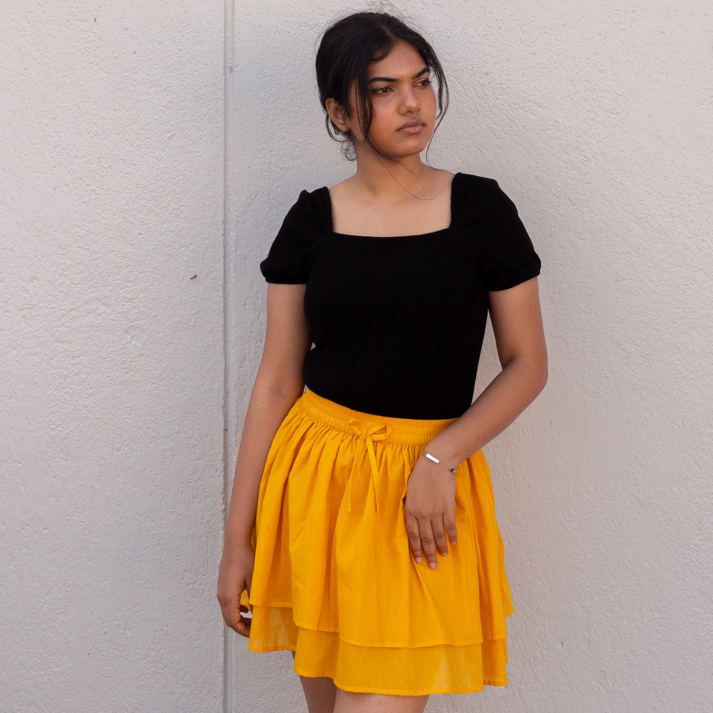 Woman wearing a black top and yellow skirt against a plain background
