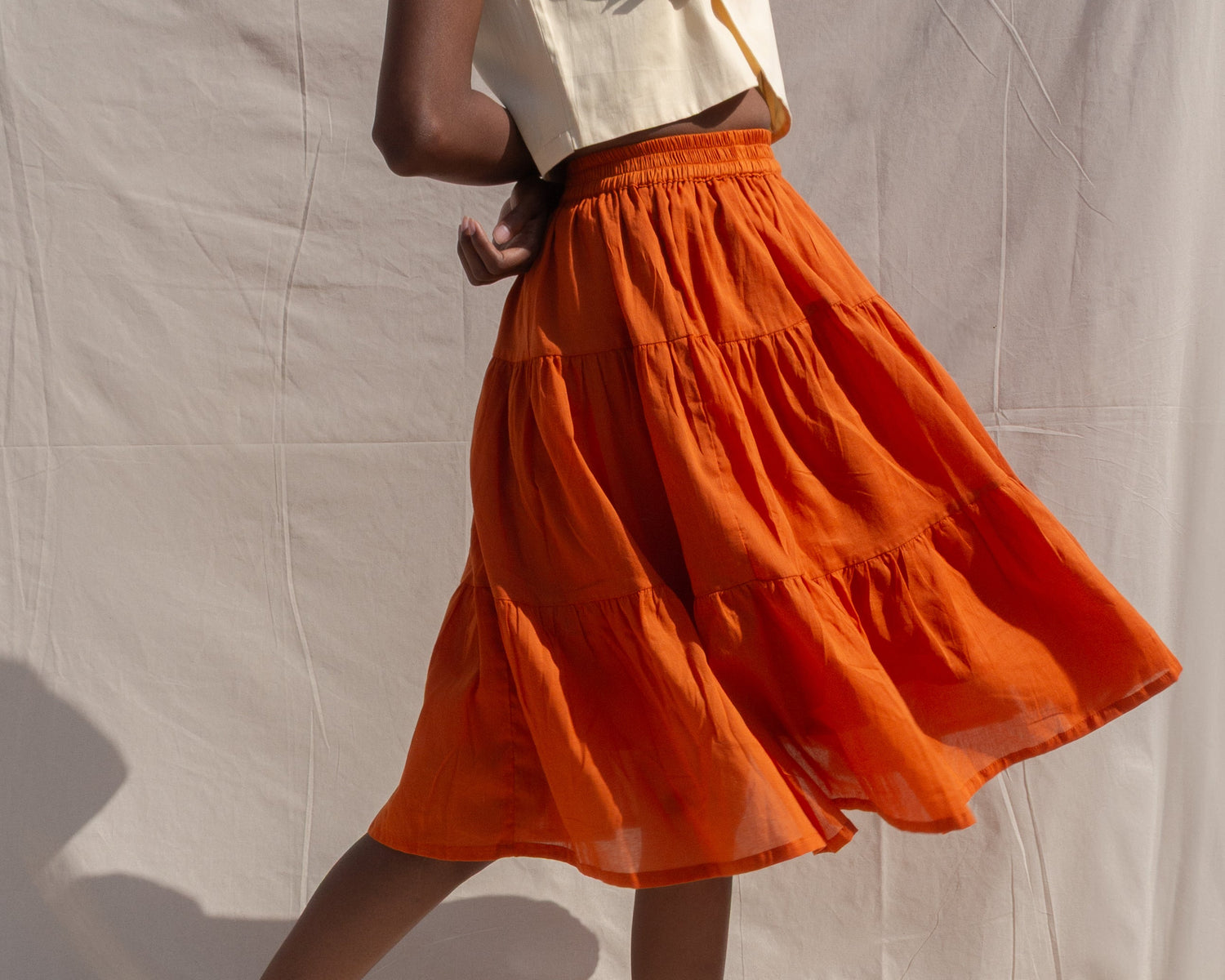 Person wearing a white top and orange skirt against a plain background