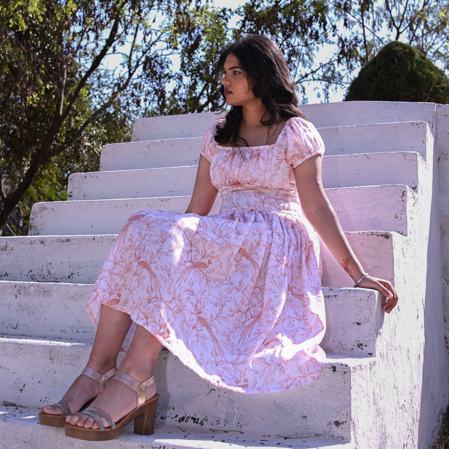Woman in a floral dress sitting on white steps with trees in the background