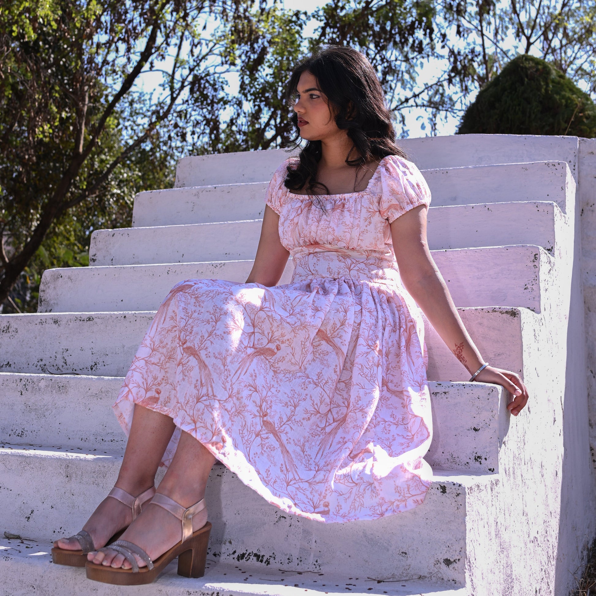 Woman in a floral dress sitting on white steps with trees in the background
