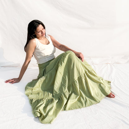 Woman wearing a white top and light green skirt sitting on a white floor.