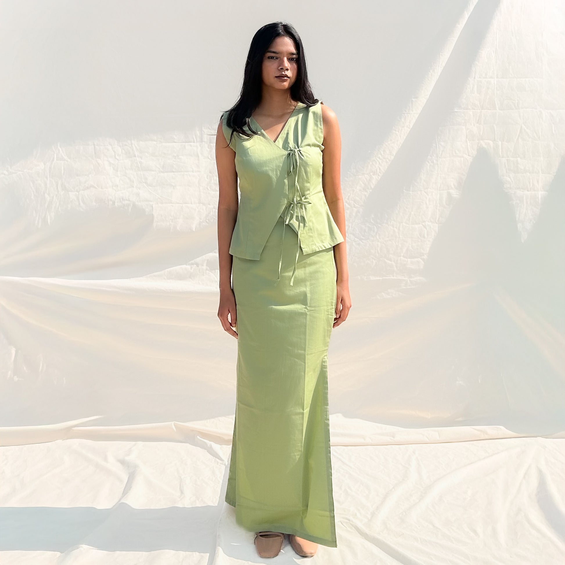 Woman wearing a light green sleeveless top and long skirt against a white background