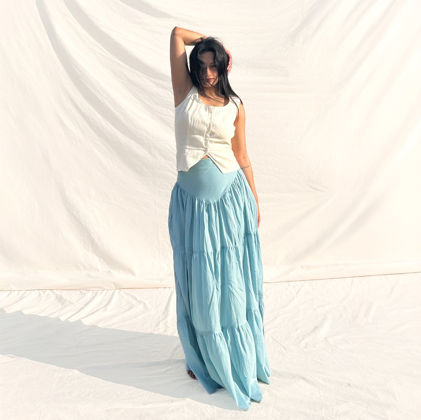 Woman wearing a white top and light blue skirt against a white background
