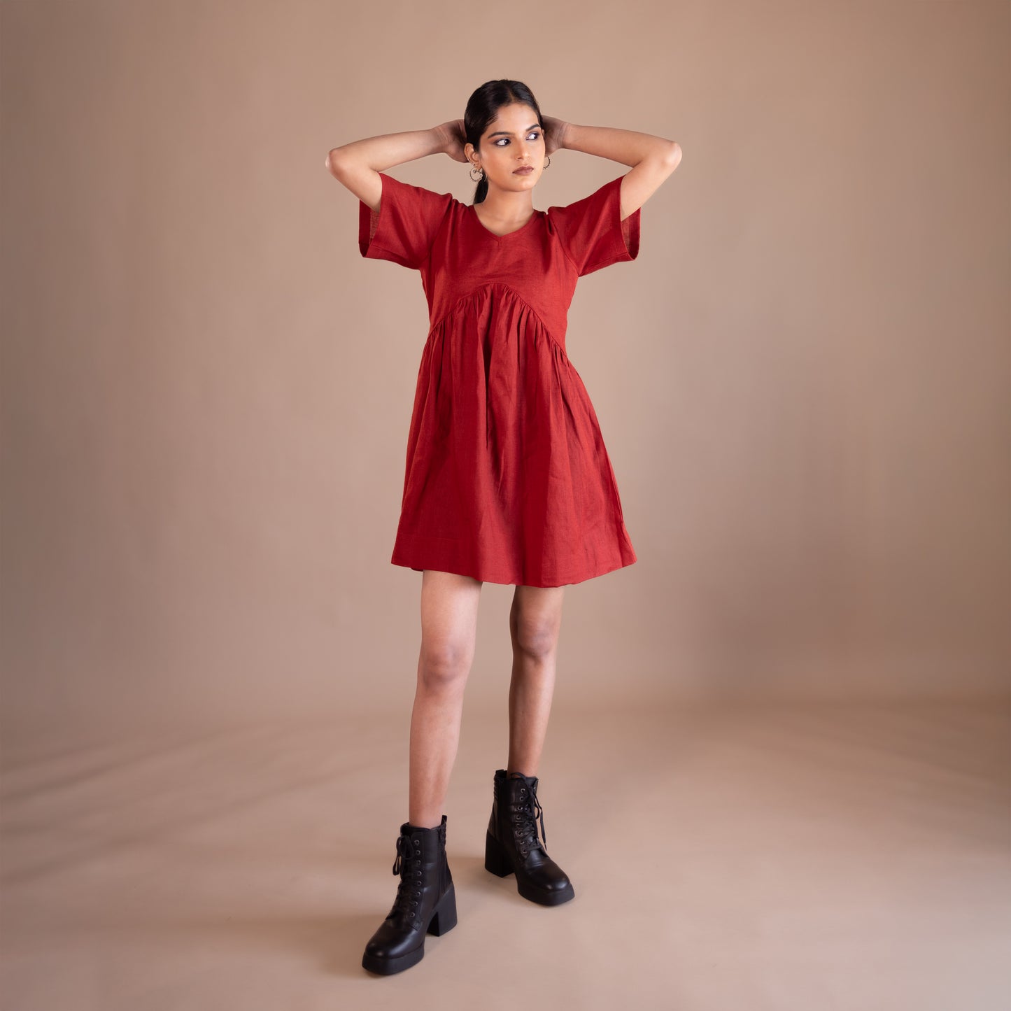 Woman wearing a red dress with black boots on a beige background