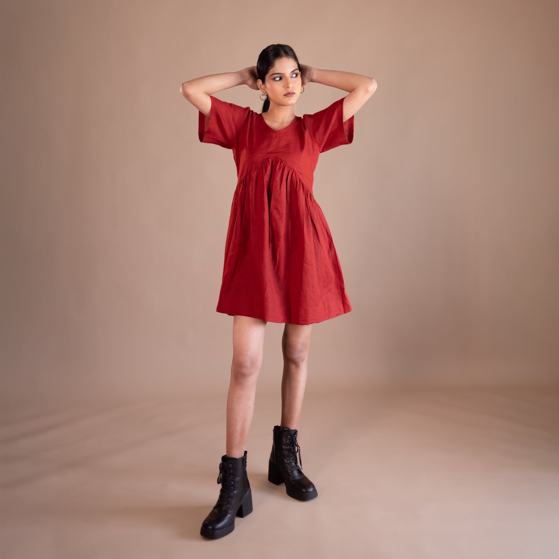 Woman wearing a red dress with black boots on a beige background