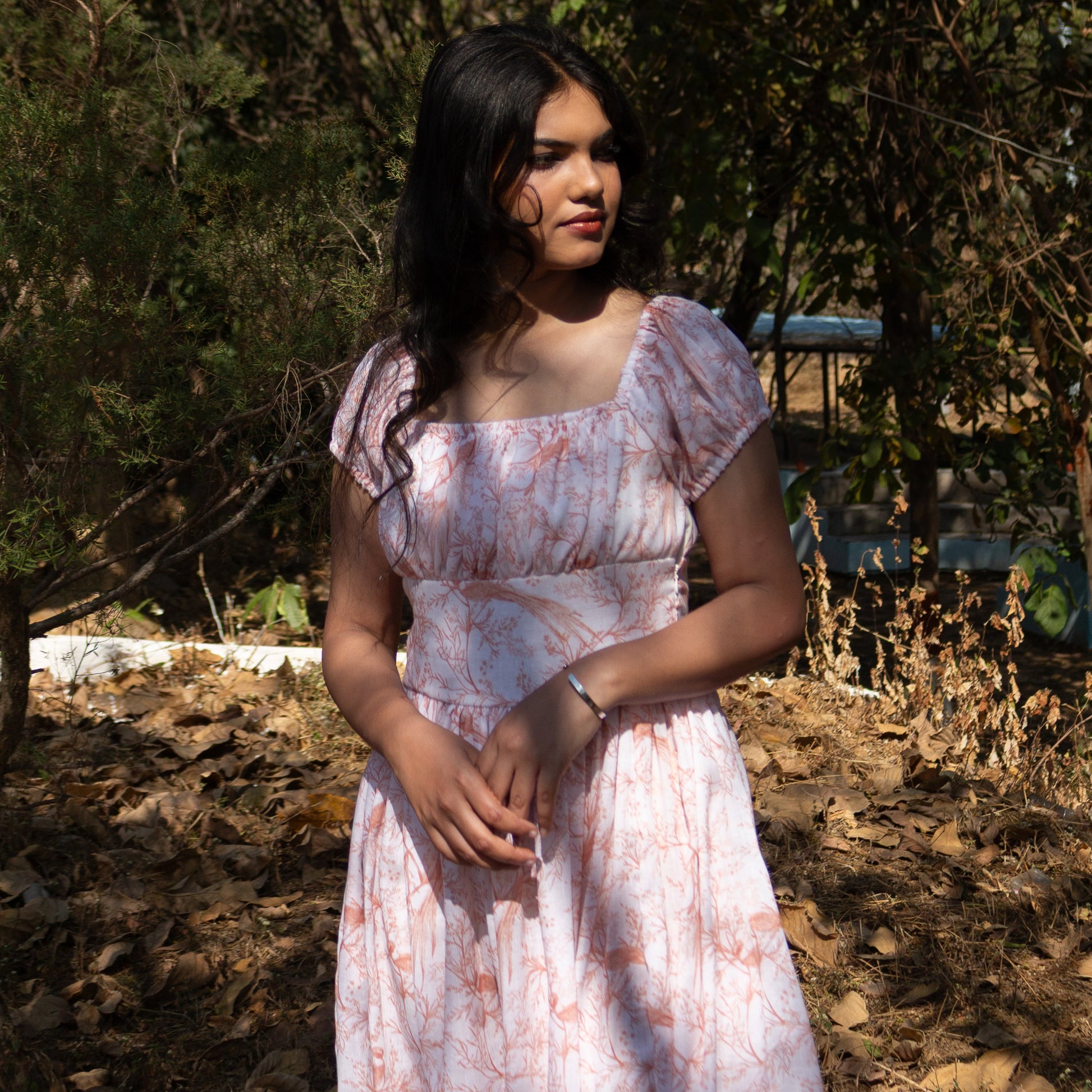 Woman in a floral dress standing outdoors with trees in the background