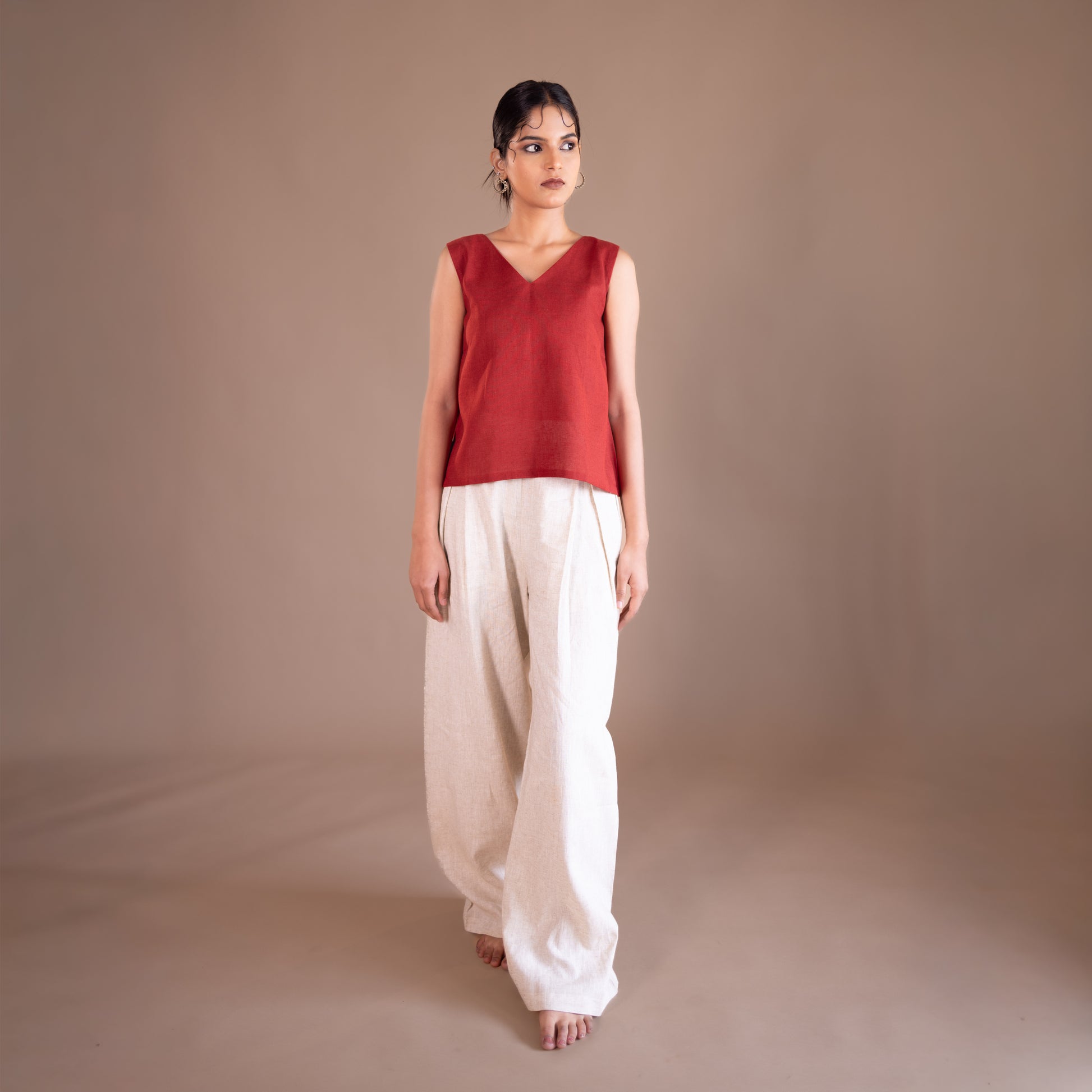 Woman wearing a red sleeveless top and white pants against a brown background