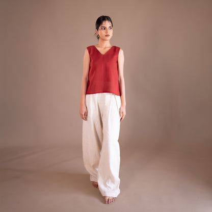 Woman wearing a red sleeveless top and white pants against a brown background