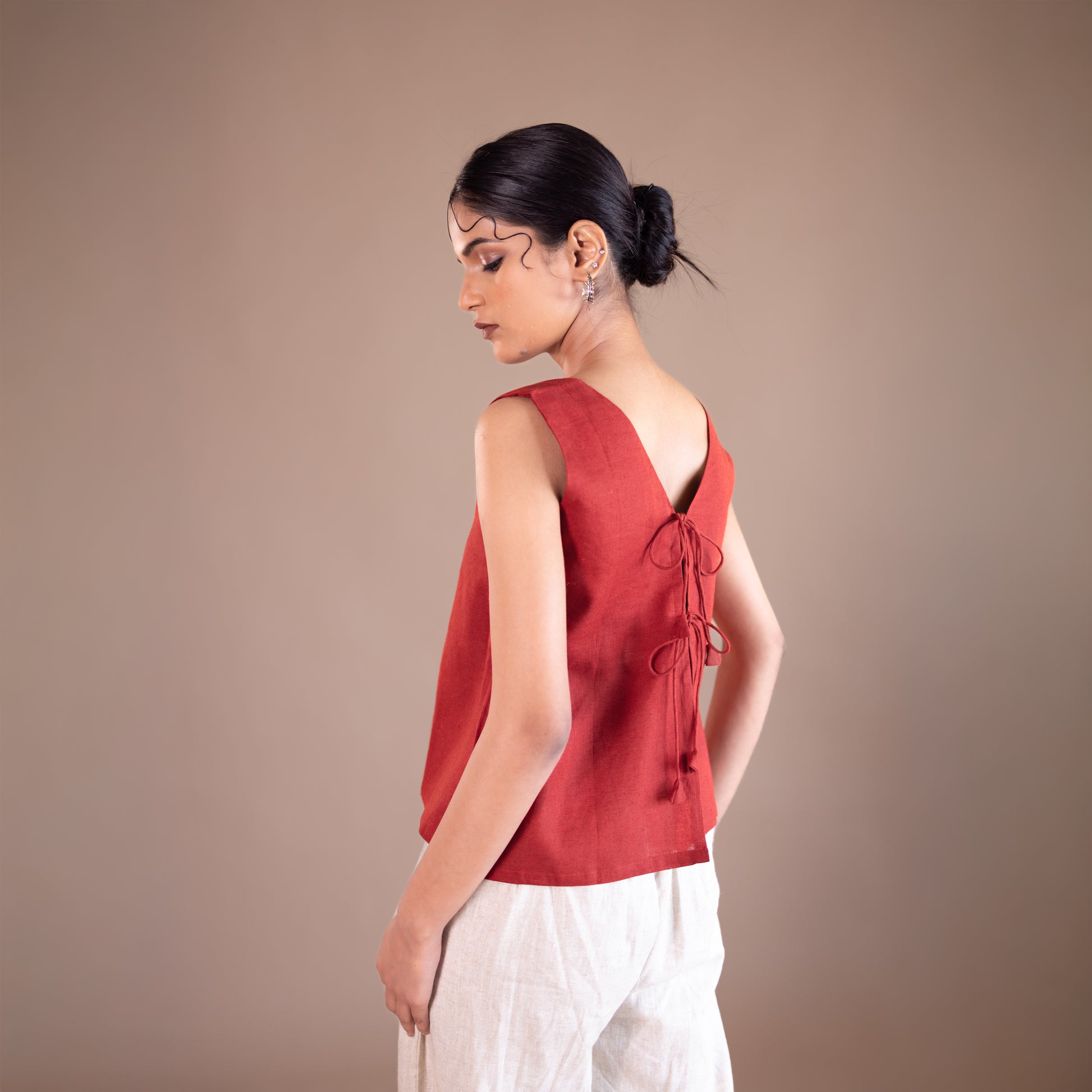 Woman wearing a red sleeveless top with a bow detail on a beige background