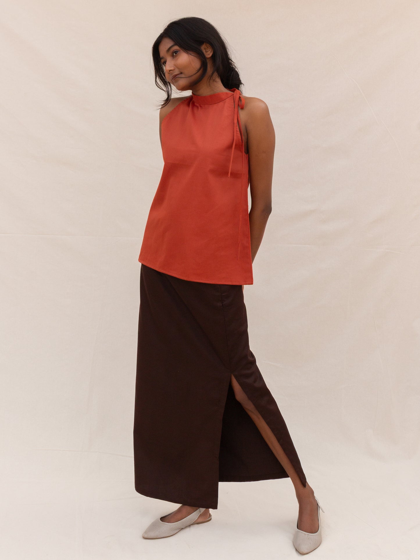 Woman wearing a red sleeveless top and brown skirt on a white background