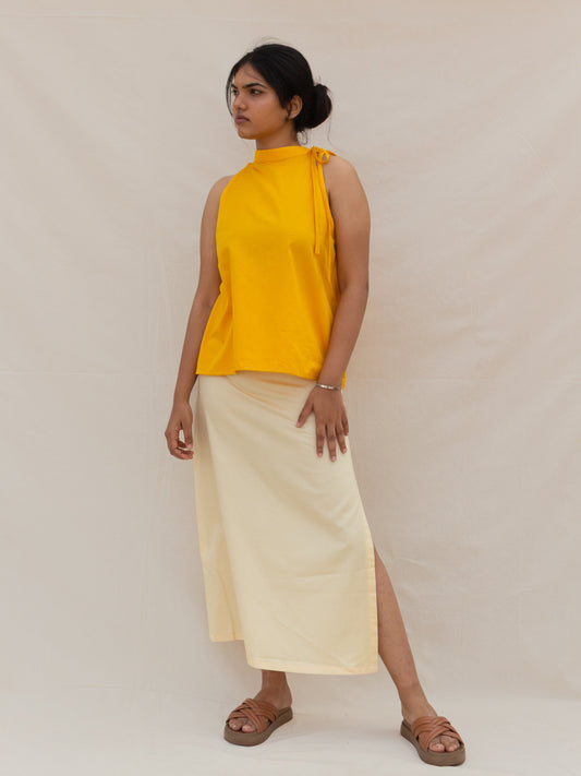 Woman wearing a yellow sleeveless top and light-colored skirt on a plain background
