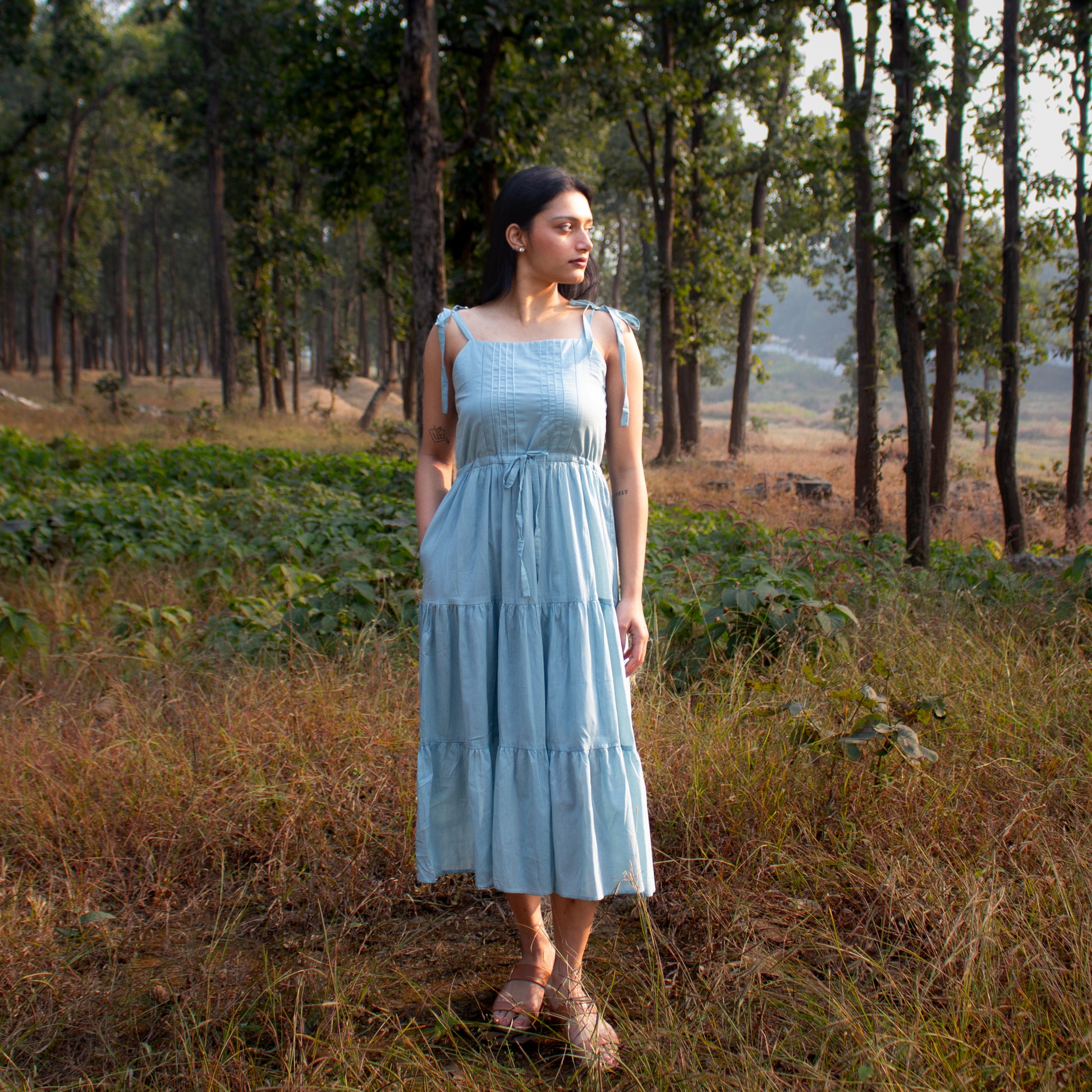 Woman in a light blue dress standing in a forest clearing