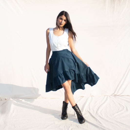 Woman wearing a white top and teal skirt with black boots on a light background