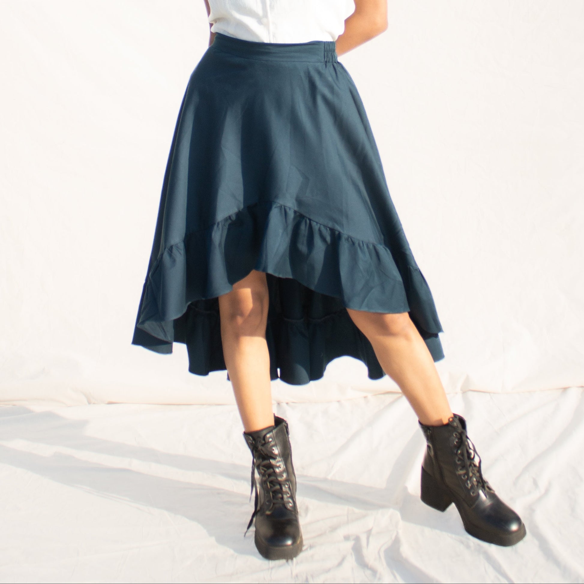 Woman wearing a white top and teal skirt with black boots on a white background