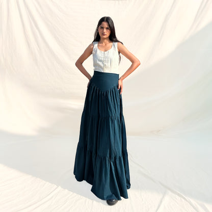 Woman wearing a white top and dark green tiered skirt against a plain background