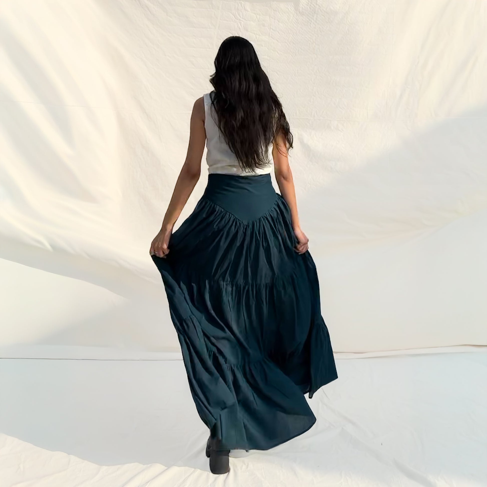 Woman wearing a long dark green skirt and white top on a plain background