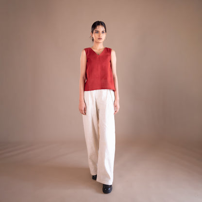 Woman wearing a red sleeveless top and white pants against a beige background