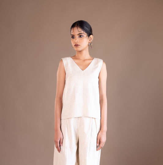Woman wearing a beige sleeveless top and wide-leg pants against a brown background