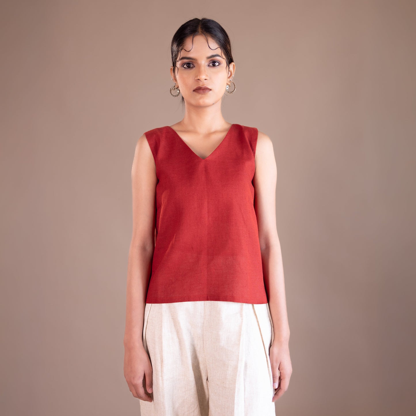 Woman wearing a red sleeveless top and beige pants against a brown background