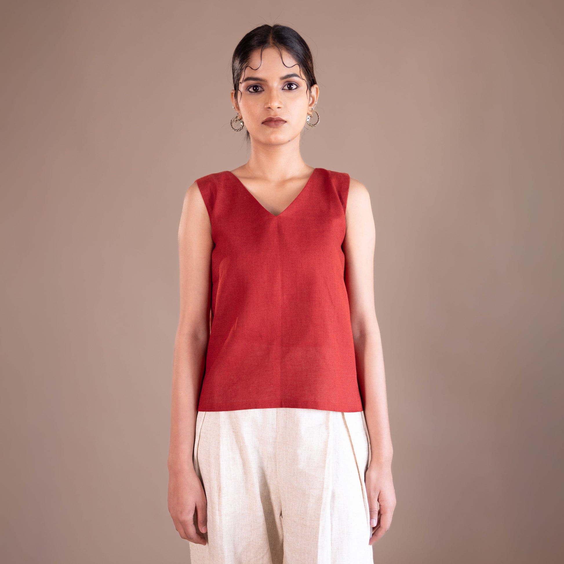 Woman wearing a red sleeveless top and beige pants against a brown background