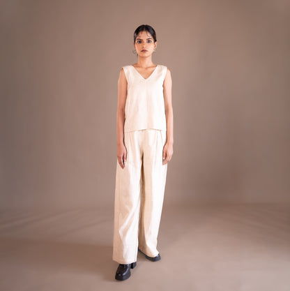 Woman wearing a beige sleeveless top and wide-leg pants against a brown background