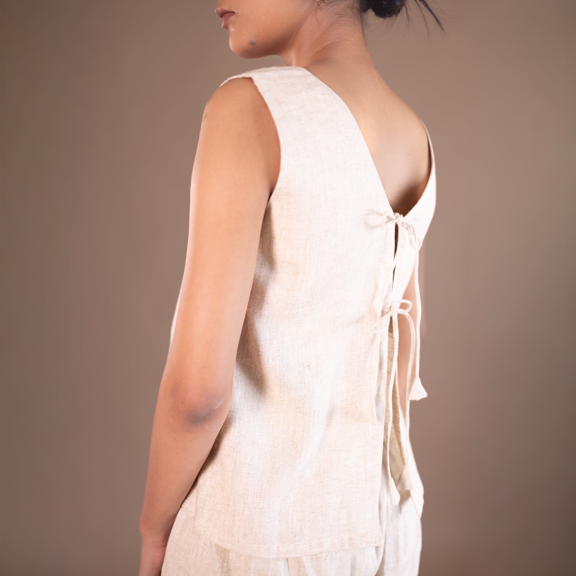 Woman wearing a light-colored sleeveless dress against a brown background