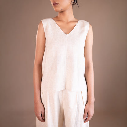 Person wearing a beige sleeveless top and pants against a brown background