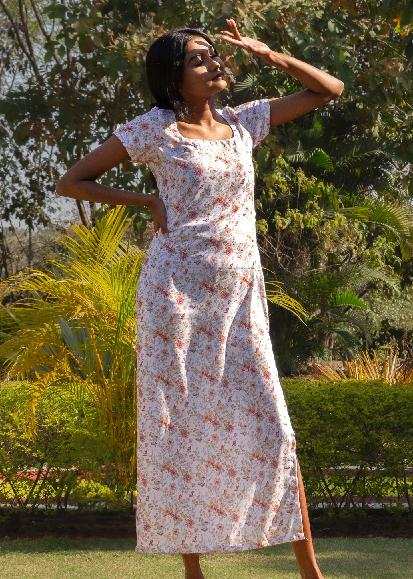 Woman in a floral dress standing outdoors with trees and greenery in the background