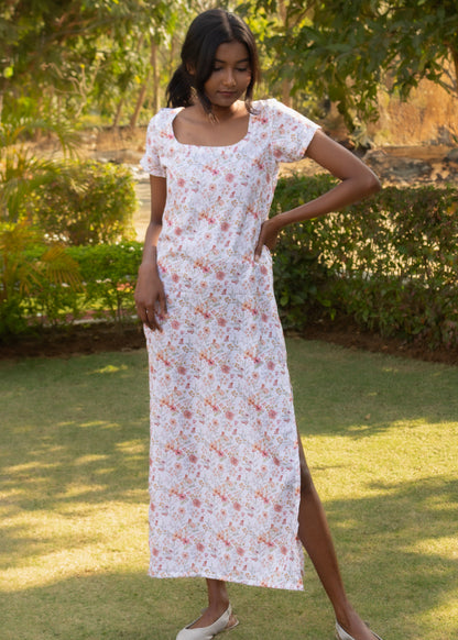 Woman in a white dress with a floral pattern standing in a garden.