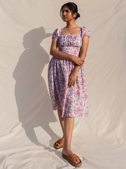 Woman wearing a floral dress standing against a plain background